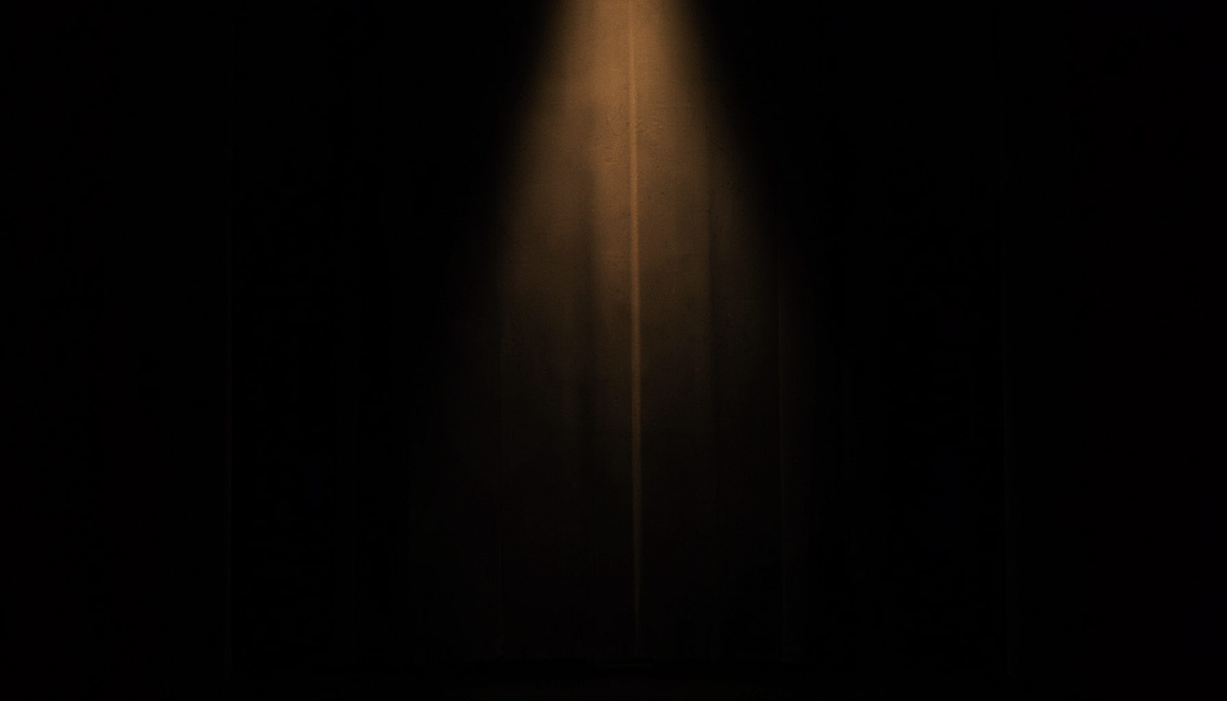 A moody portrait-style backdrop in deep charcoal black with a single warm amber spotlight glow, evoking an old cinema stage curtain, calm and nostalgic in mood
