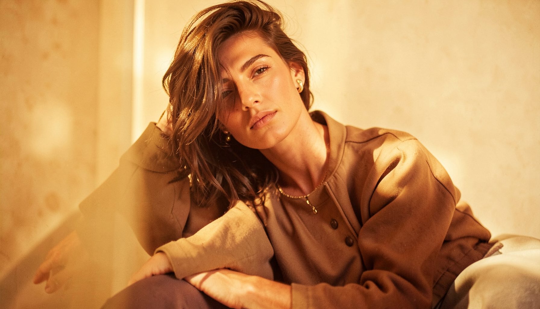 Candid-style modelling shot with warm amber and cream hues, relaxed pose